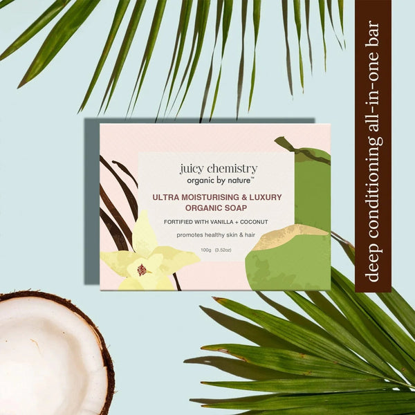 Juicy Chemistry Ultra Moisturising and Luxury Organic Soap box fortified with vanilla and coconut beside palm leaves and a halved coconut, labeled deep conditioning all-in-one bar, 100g