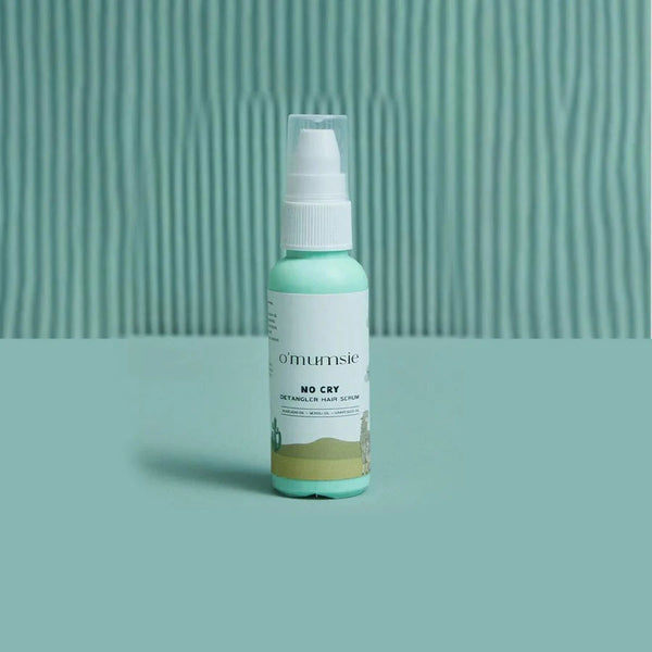 O'mumsie No Cry Detangler Hair Serum bottle standing on teal textured background, made with avocado oil, neroli oil, and grapeseed oil