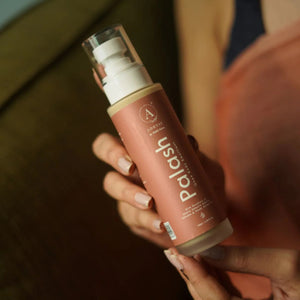 Woman holding Adhyay Palash Ghee Body Emollient bottle in a cozy lifestyle setting