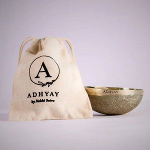 Adhyay Kansa Vatki bronze bowl next to its cotton drawstring storage pouch printed with the Adhyay by Nabhi Sutra log