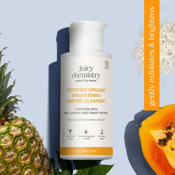 Juicy Chemistry Certified Organic Brightening Enzyme Cleanser bottle between pineapple and papaya halves with orange banner text gently exfoliates and brightens
