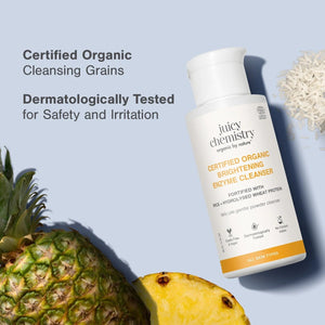 Juicy Chemistry Certified Organic Brightening Enzyme Cleanser bottle with fresh pineapple and rice grains, labeled Certified Organic Cleansing Grains and Dermatologically Tested for Safety and Irritation
