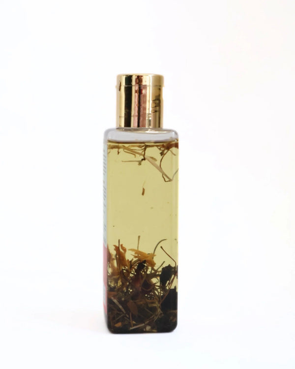 Close-up of Sampoorna Hair Oil bottle showing visible whole herbs infused in golden oil