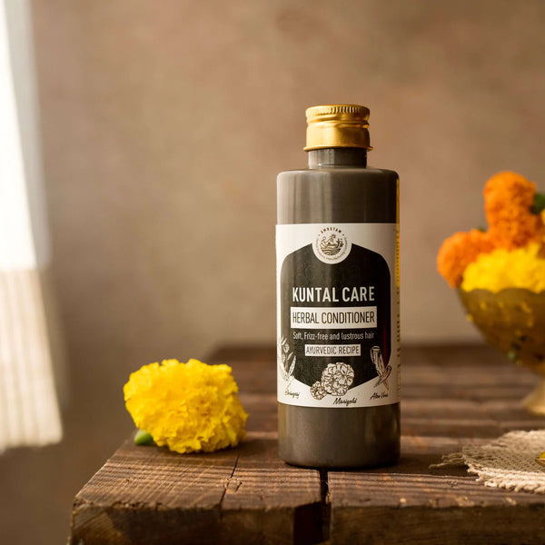 Kuntal Care Herbal Conditioner bottle with gold cap on rustic wooden surface, surrounded by yellow and orange marigold flowers – Ayurvedic hair conditioner for frizz control and deep hydration
